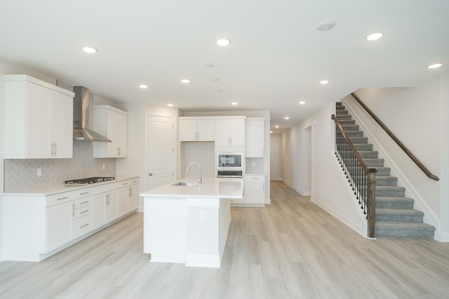 kitchen with wall chimney range hood, a kitchen island with sink, black microwave, white cabinets, and stainless steel gas stovetop