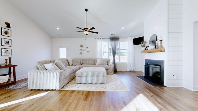 living room featuring ceiling fan, lofted ceiling, a fireplace, and light hardwood / wood-style flooring