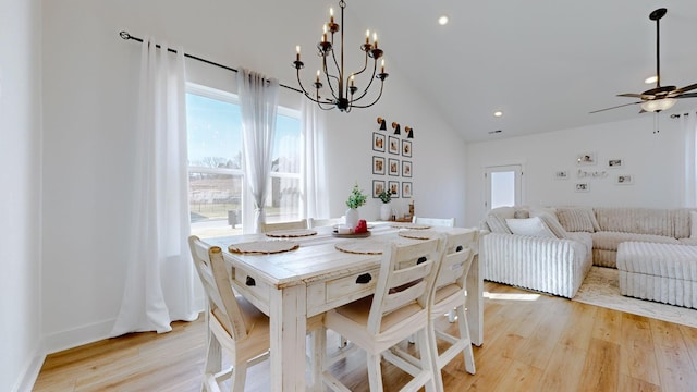 dining area featuring ceiling fan with notable chandelier, vaulted ceiling, and light hardwood / wood-style flooring