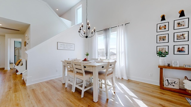 dining space featuring a towering ceiling, an inviting chandelier, and light wood-type flooring