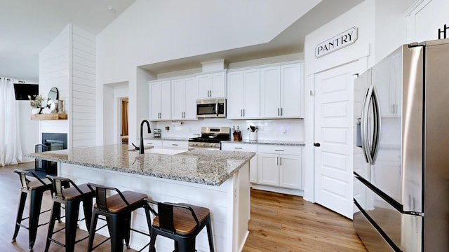 kitchen with sink, a breakfast bar area, appliances with stainless steel finishes, an island with sink, and white cabinets