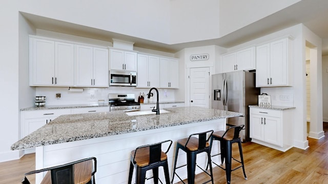 kitchen with white cabinetry, an island with sink, sink, stainless steel appliances, and light hardwood / wood-style flooring