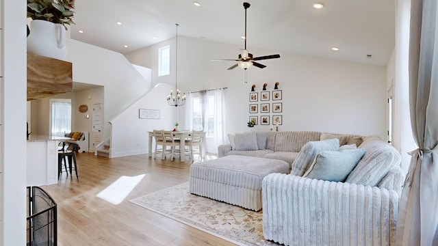 living room with ceiling fan with notable chandelier, light hardwood / wood-style floors, and a high ceiling