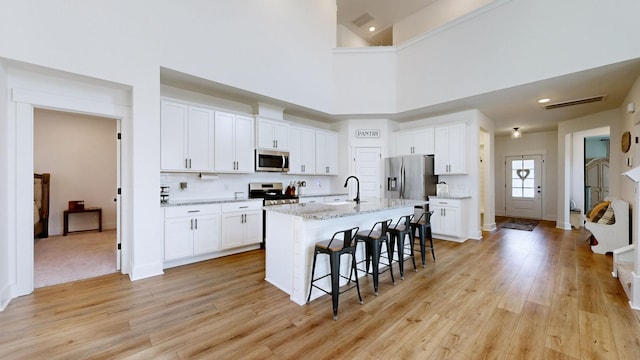 kitchen featuring white cabinetry, stainless steel appliances, a kitchen island with sink, and a breakfast bar area