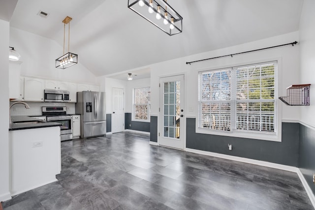 interior space with sink, white cabinetry, hanging light fixtures, stainless steel appliances, and decorative backsplash