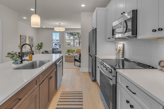 kitchen with appliances with stainless steel finishes, white cabinetry, sink, hanging light fixtures, and light hardwood / wood-style flooring