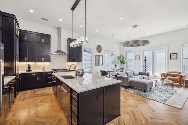 kitchen with pendant lighting, an island with sink, sink, light parquet flooring, and wall chimney range hood