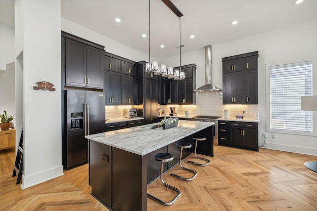 kitchen featuring pendant lighting, wall chimney range hood, a breakfast bar, high quality appliances, and a center island with sink