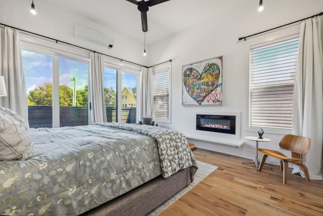 bedroom featuring an AC wall unit, multiple windows, access to exterior, ceiling fan, and light hardwood / wood-style flooring