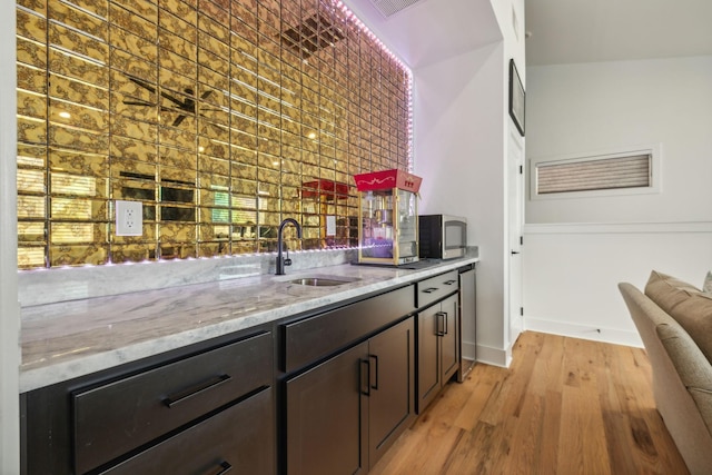 kitchen featuring light stone countertops, dark brown cabinets, sink, and light hardwood / wood-style floors