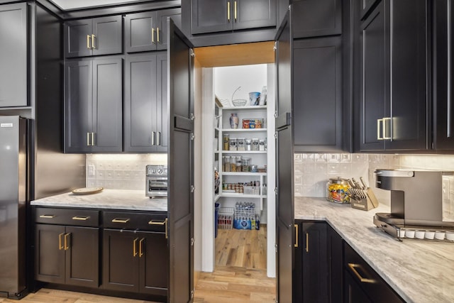 kitchen featuring light stone countertops, decorative backsplash, refrigerator, and light hardwood / wood-style flooring