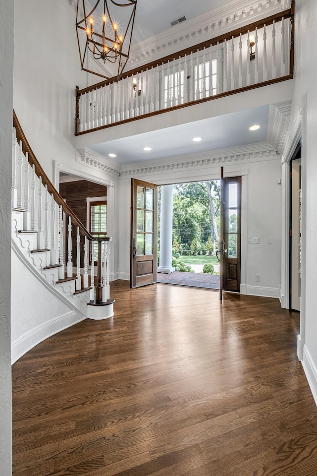 entrance foyer with ornamental molding, a towering ceiling, a chandelier, and dark hardwood / wood-style flooring