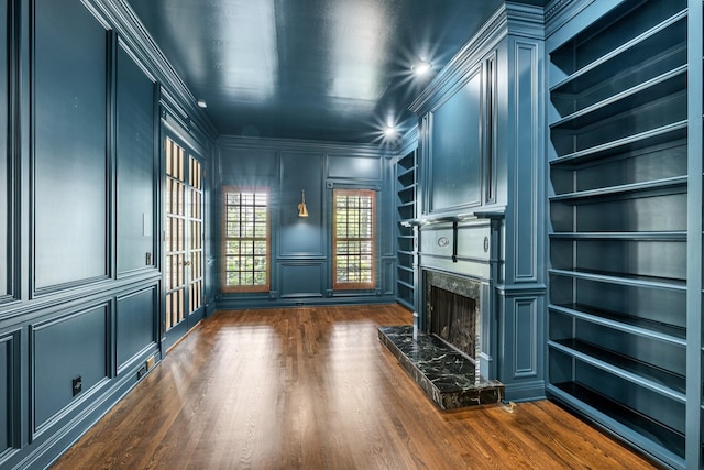 interior space featuring dark wood-type flooring, ornamental molding, a premium fireplace, and built in features