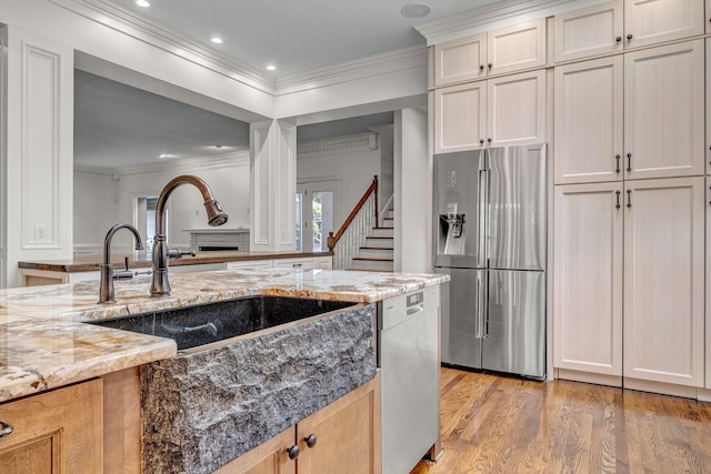 kitchen with sink, stainless steel appliances, crown molding, light stone countertops, and light hardwood / wood-style flooring