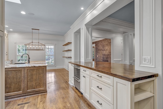 kitchen featuring white cabinetry, butcher block counters, sink, hanging light fixtures, and a kitchen island with sink