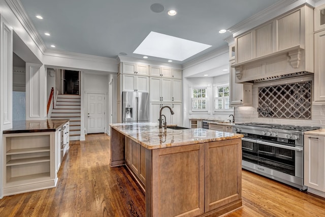 kitchen featuring sink, light stone counters, a skylight, a center island with sink, and appliances with stainless steel finishes