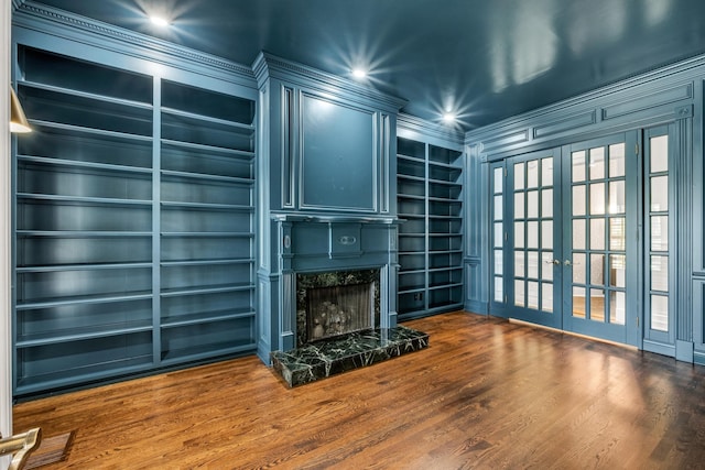 living room with french doors, crown molding, built in features, hardwood / wood-style flooring, and a premium fireplace