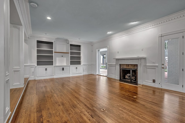 unfurnished living room featuring crown molding, wood-type flooring, a premium fireplace, and built in features