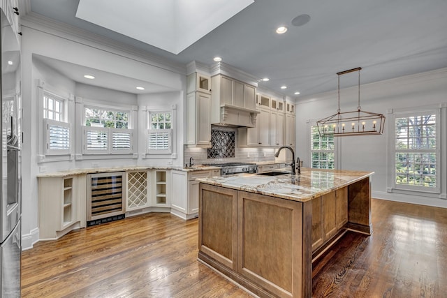 kitchen featuring sink, stove, wine cooler, light stone countertops, and a center island with sink