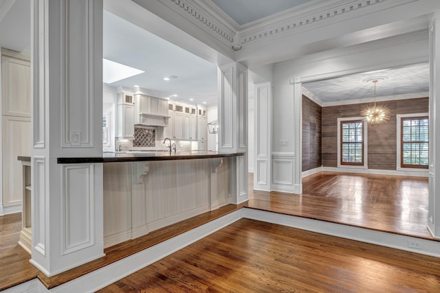 kitchen featuring white cabinets, a chandelier, hanging light fixtures, crown molding, and dark wood-type flooring