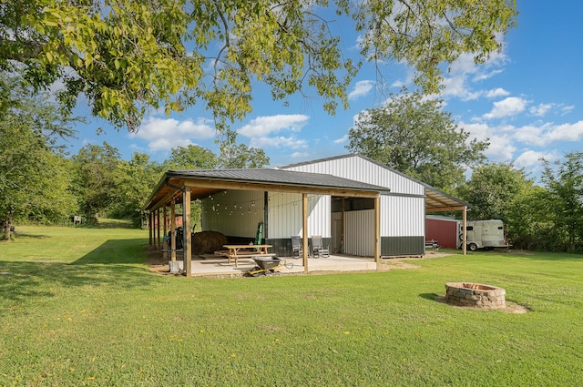 rear view of house featuring an outbuilding, a lawn, and a fire pit