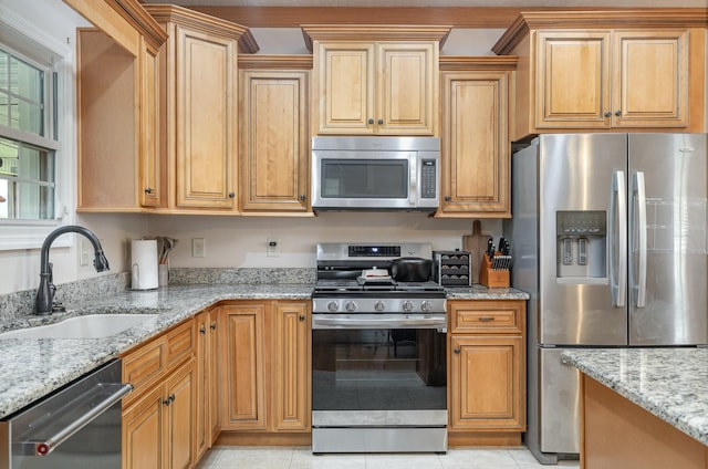 kitchen with appliances with stainless steel finishes, light stone countertops, sink, and light tile patterned floors