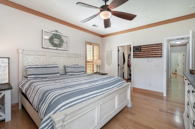 bedroom featuring ceiling fan, a walk in closet, ornamental molding, and light hardwood / wood-style flooring