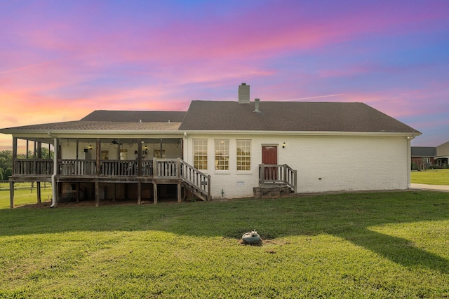 back house at dusk featuring a wooden deck, a yard, and a sunroom