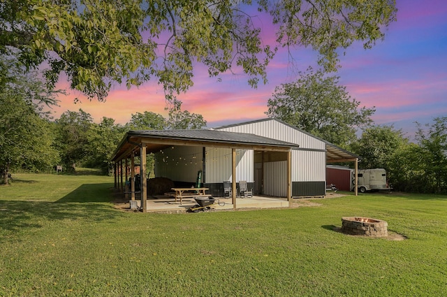 back house at dusk with an outdoor structure, a lawn, and an outdoor fire pit