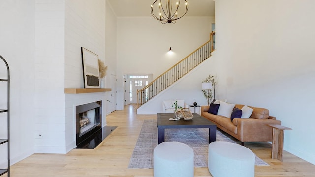 living room with a towering ceiling, a large fireplace, a chandelier, crown molding, and light wood-type flooring