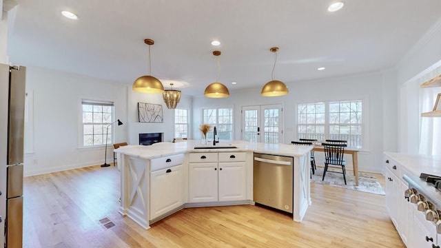 kitchen with appliances with stainless steel finishes, decorative light fixtures, white cabinetry, sink, and a center island with sink