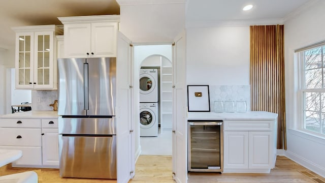 kitchen with stainless steel refrigerator, stacked washer / dryer, white cabinets, wine cooler, and crown molding