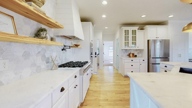 kitchen featuring stainless steel refrigerator, white cabinets, gas range gas stove, light stone countertops, and light hardwood / wood-style flooring