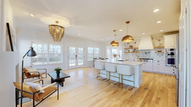 kitchen with french doors, an island with sink, custom range hood, and white cabinets