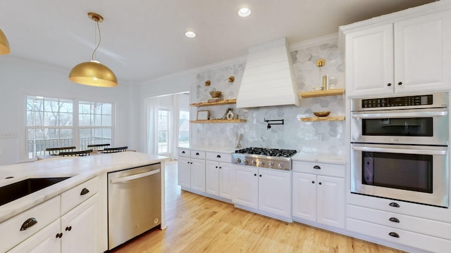 kitchen featuring premium range hood, appliances with stainless steel finishes, pendant lighting, white cabinets, and ornamental molding