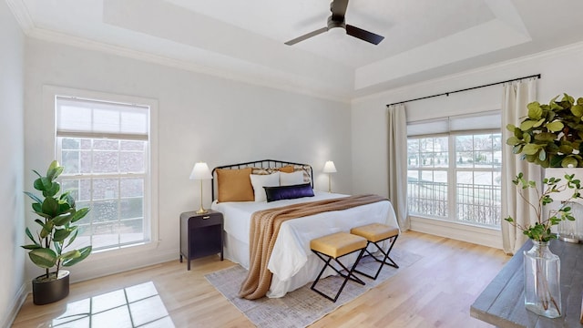 bedroom with ceiling fan, ornamental molding, a tray ceiling, and light hardwood / wood-style floors