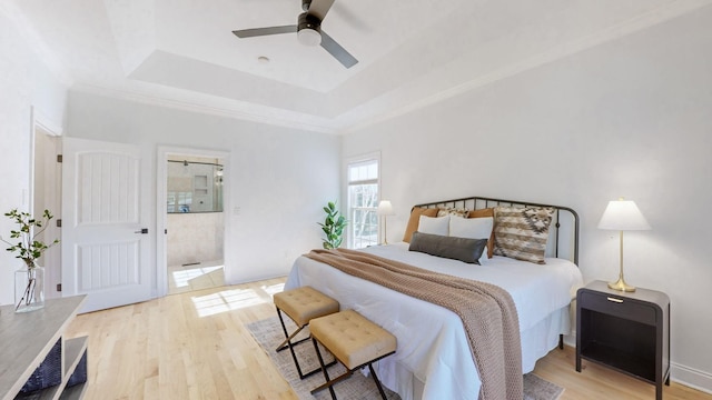 bedroom featuring ceiling fan, connected bathroom, a tray ceiling, and light hardwood / wood-style floors