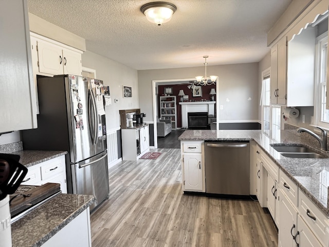 kitchen featuring white cabinetry, sink, hanging light fixtures, stainless steel appliances, and light hardwood / wood-style flooring