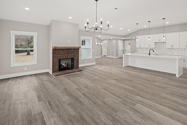 unfurnished living room with plenty of natural light, a fireplace, light hardwood / wood-style floors, and a notable chandelier