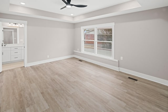 unfurnished bedroom featuring a raised ceiling, ceiling fan, ensuite bath, and light hardwood / wood-style floors