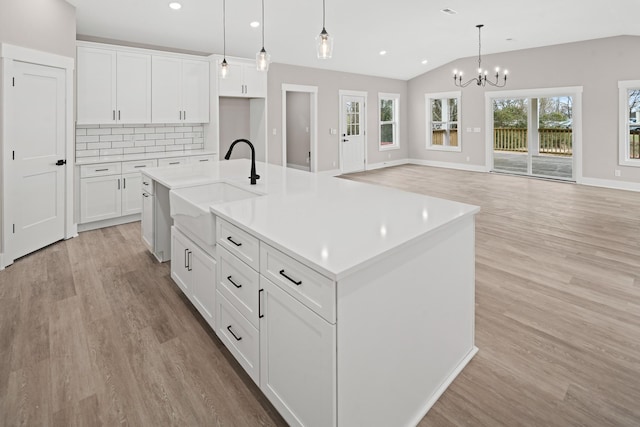 kitchen featuring an island with sink, sink, white cabinets, and decorative light fixtures