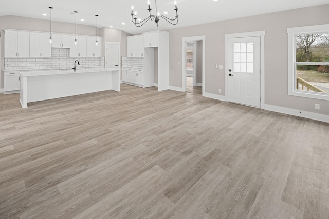 unfurnished living room featuring sink, a chandelier, and light hardwood / wood-style floors