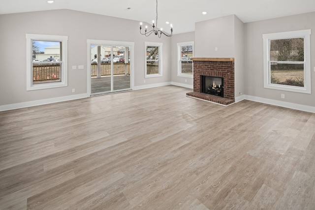 unfurnished living room with lofted ceiling, a fireplace, a healthy amount of sunlight, and light wood-type flooring