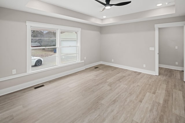 spare room with light hardwood / wood-style flooring, a raised ceiling, and ceiling fan