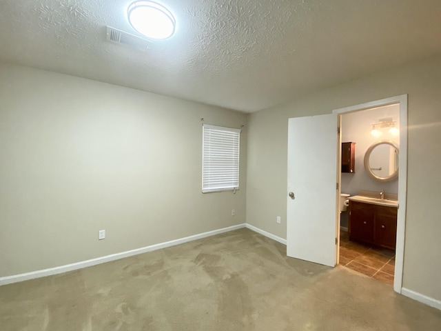 unfurnished bedroom featuring ensuite bathroom, sink, light colored carpet, and a textured ceiling