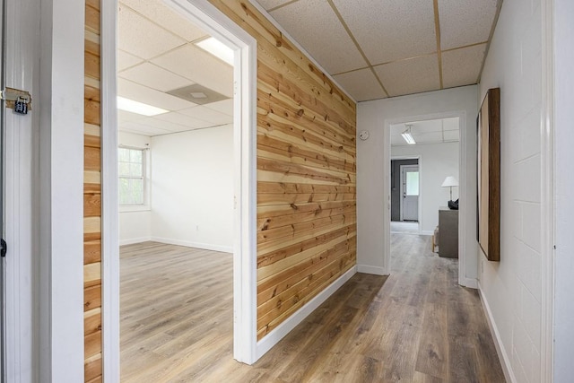 corridor featuring a paneled ceiling, wood-type flooring, and wood walls