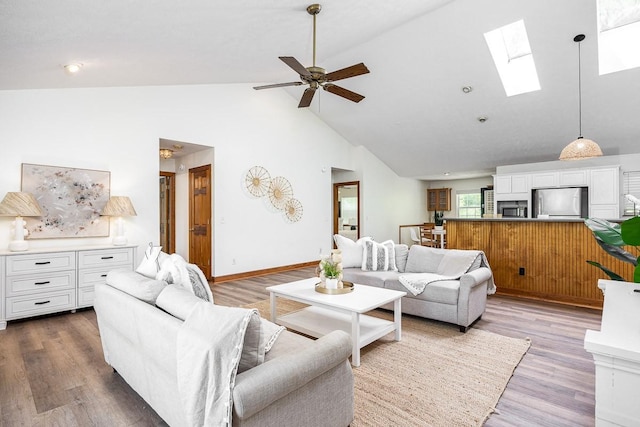 living room with ceiling fan, wood-type flooring, a skylight, and high vaulted ceiling