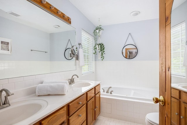 bathroom featuring vanity, tiled tub, toilet, and a healthy amount of sunlight