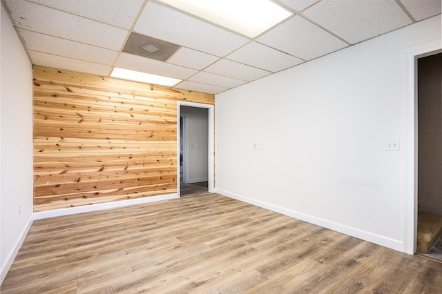 empty room with hardwood / wood-style floors, a paneled ceiling, and wooden walls