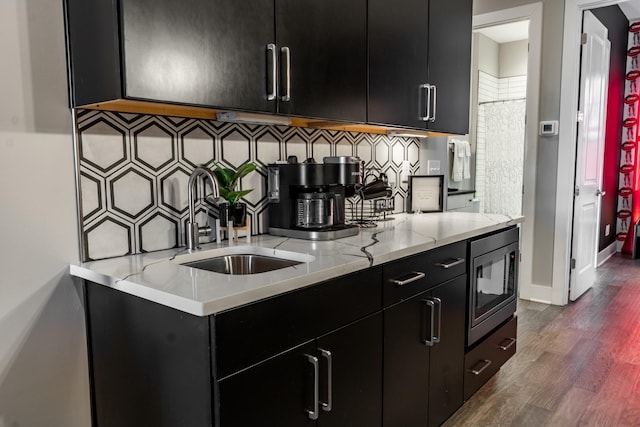 kitchen with sink, dark wood-type flooring, backsplash, stainless steel microwave, and light stone counters